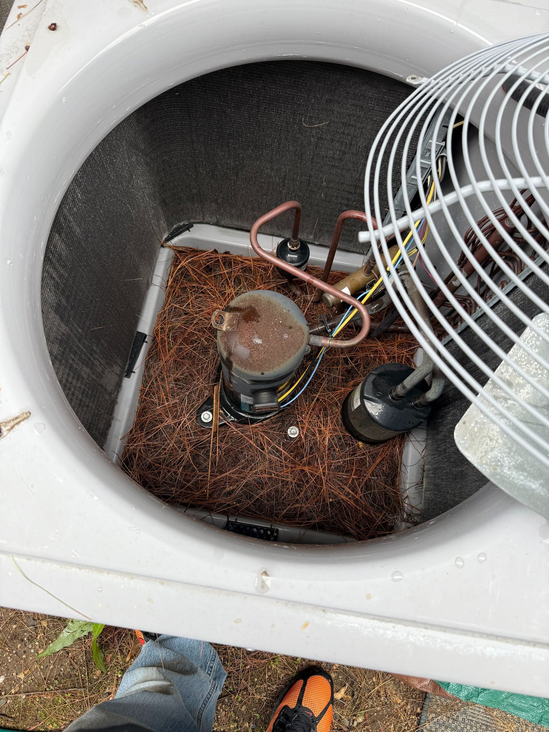 AC unit's interior with fan, compressor, and copper piping surrounded by mulch-like material.