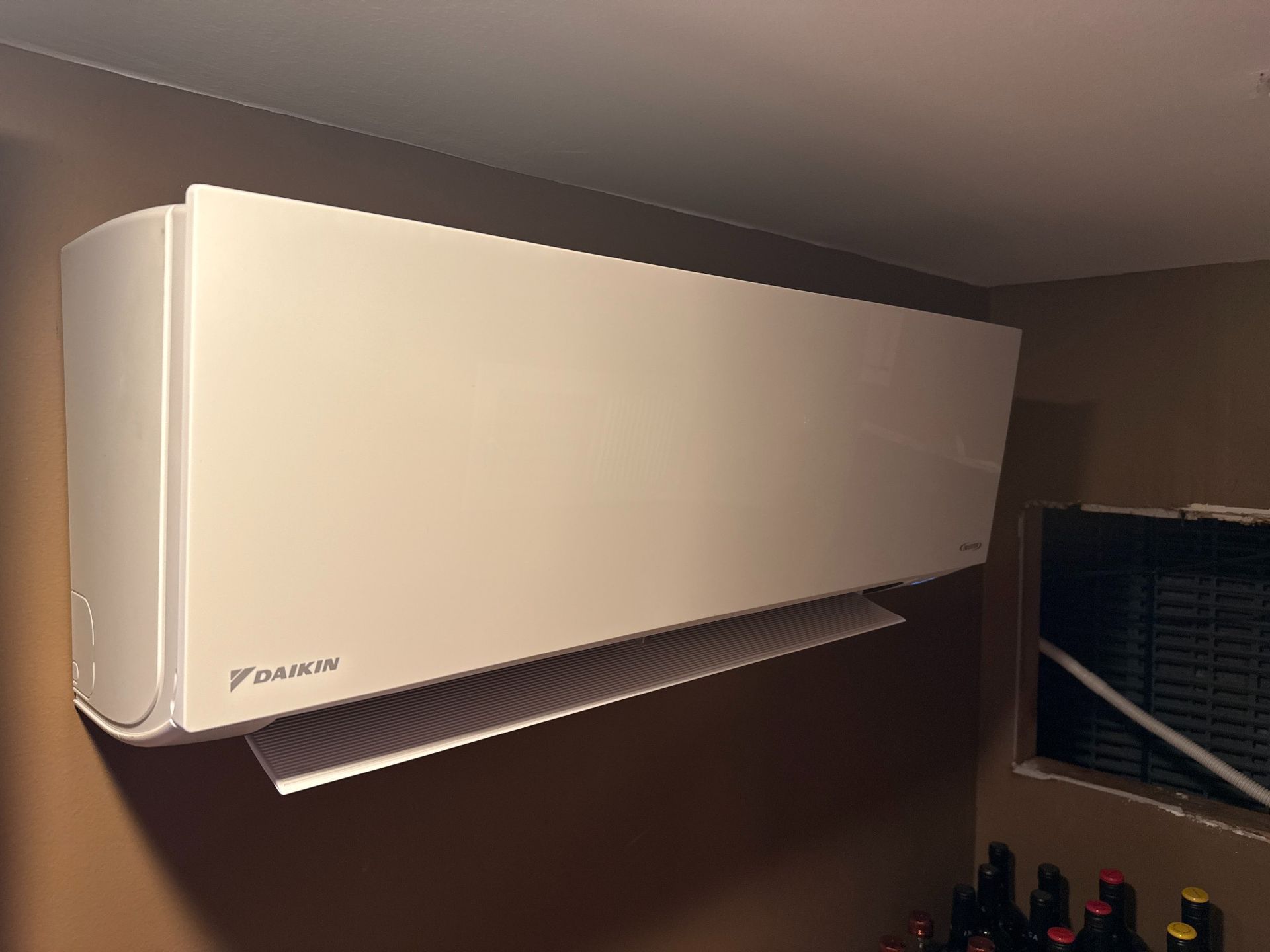Daikin wall-mounted air conditioner on a brown wall. The unit is white with a silver vent.