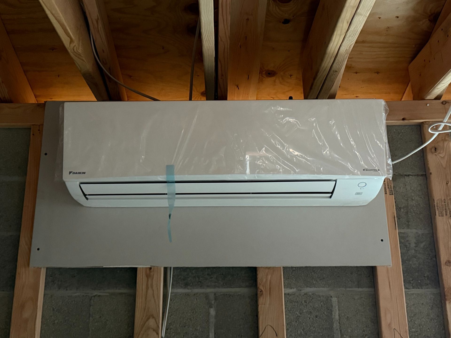 Daikin air conditioner unit on a gray wall, installed in a wooden frame under a ceiling.