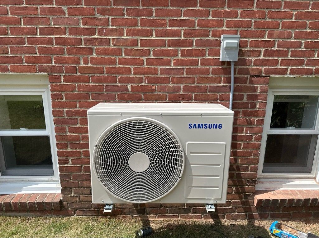 Samsung AC unit mounted on a red brick wall, between two windows.