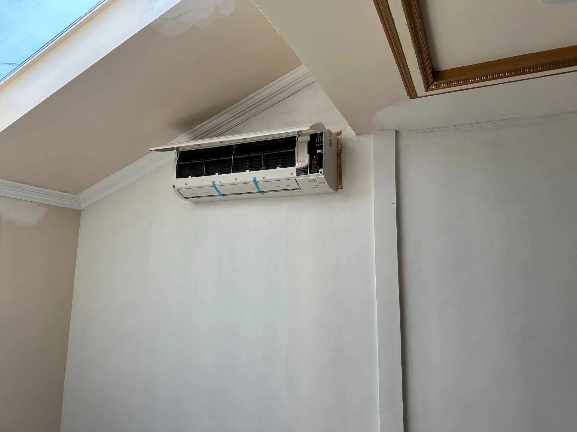 An air conditioner mounted on a white wall with decorative molding.