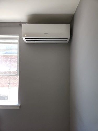 White air conditioning unit mounted on a gray wall, next to a window.
