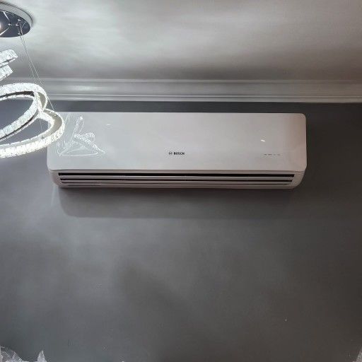 White Bosch air conditioner mounted on a gray wall, below a chandelier.