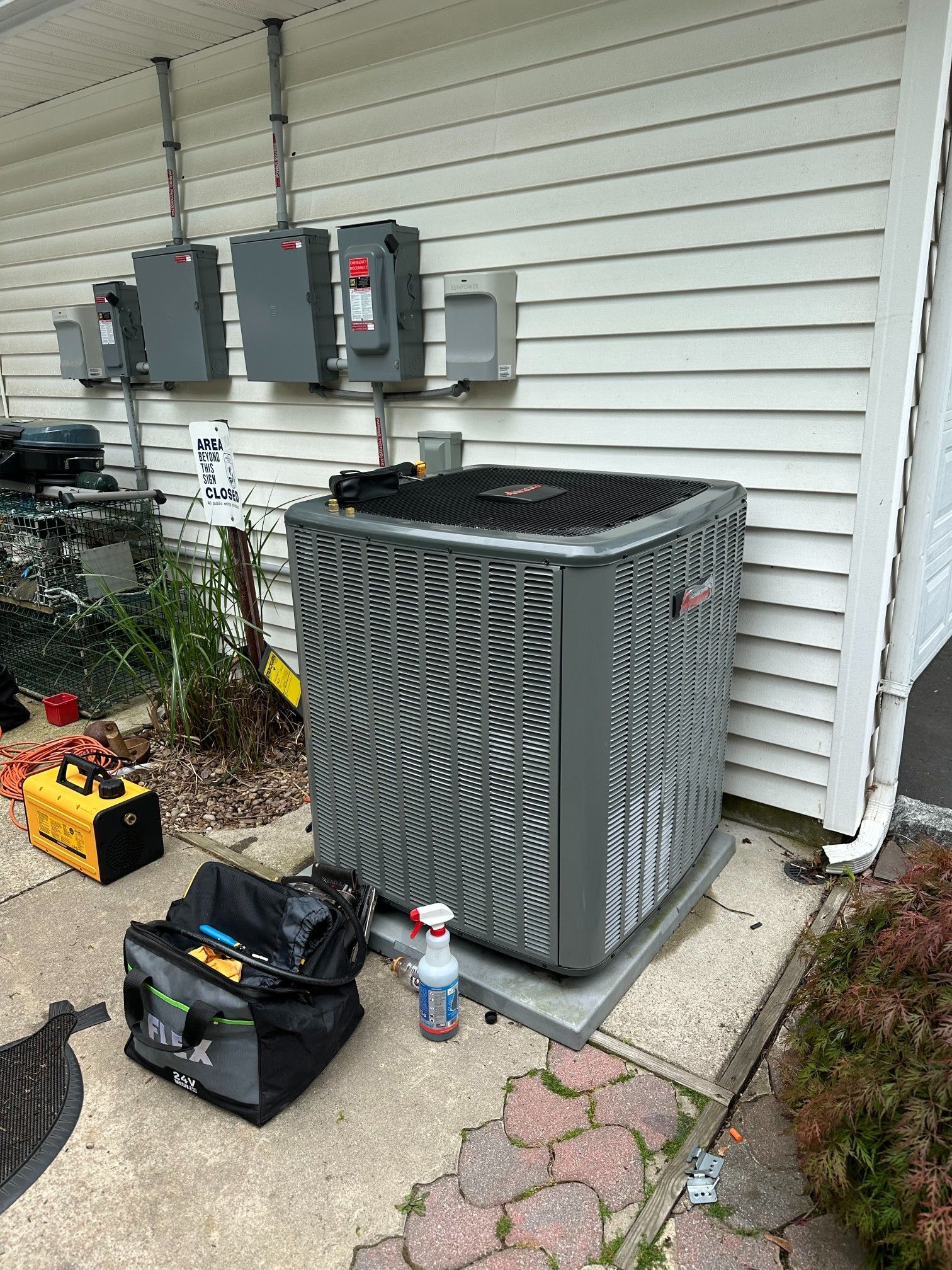 HVAC unit outside a building, with tools and electrical boxes nearby.