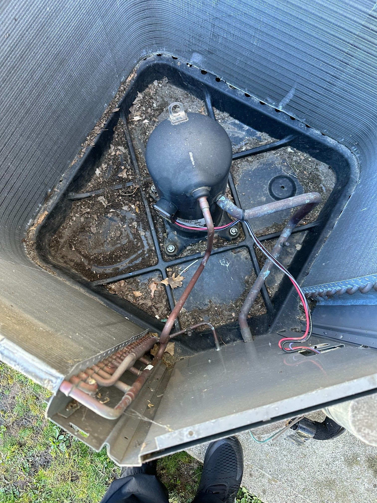 Inside an air conditioner unit: compressor, copper tubing, debris, and black base.