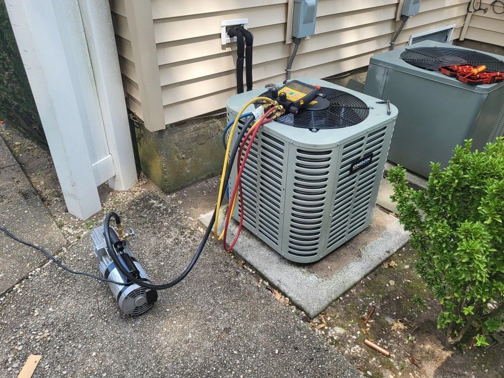 AC unit being serviced outdoors, connected to gauges and a vacuum pump on concrete.