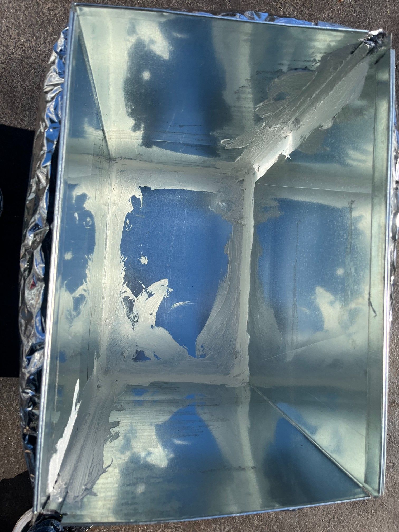 Top-down view of a metal box lined with white material, possibly sealant. Outside wrapped in foil.