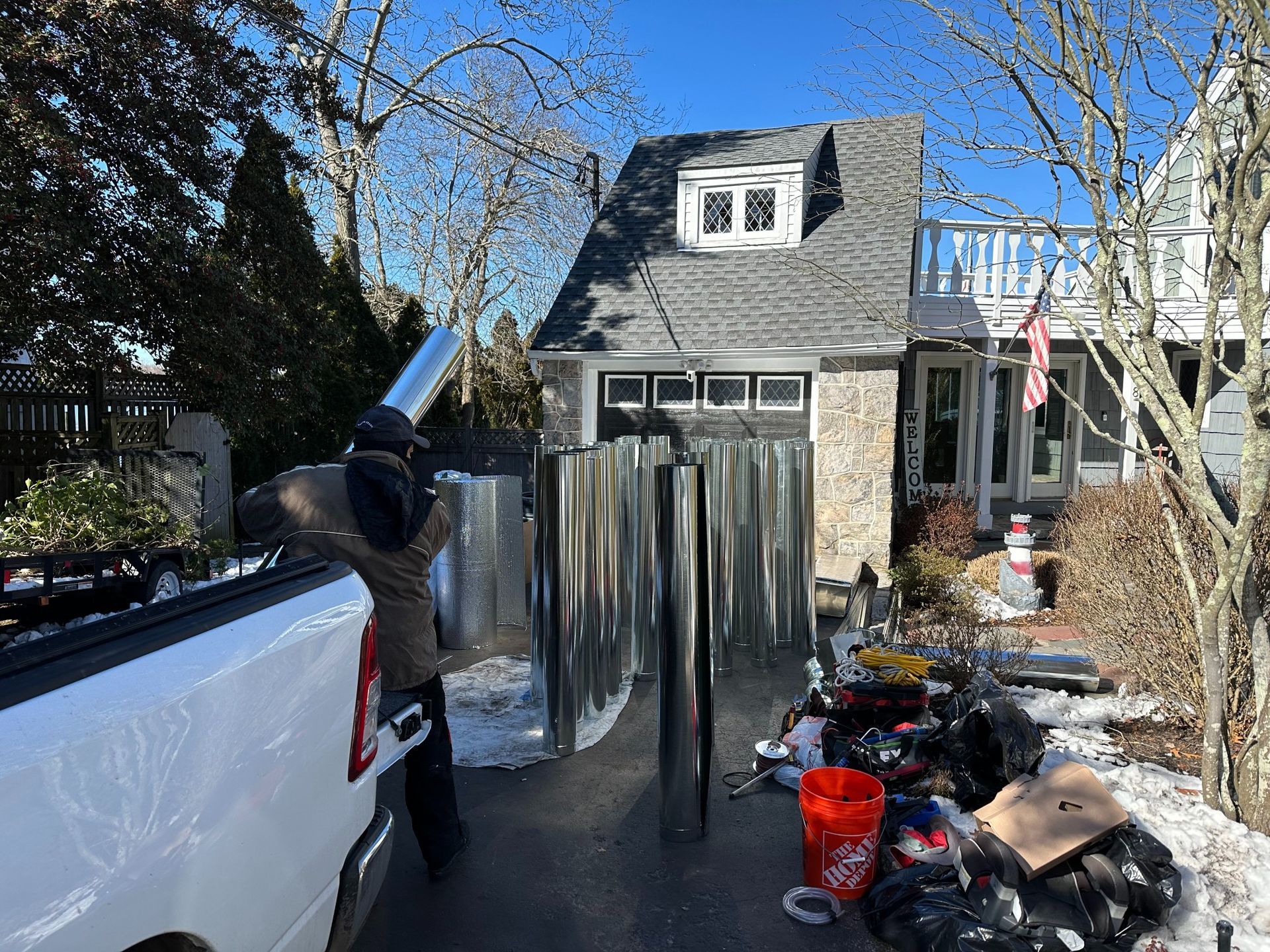 Person unloading metal sheets and a chimney pipe from a truck in front of a house.