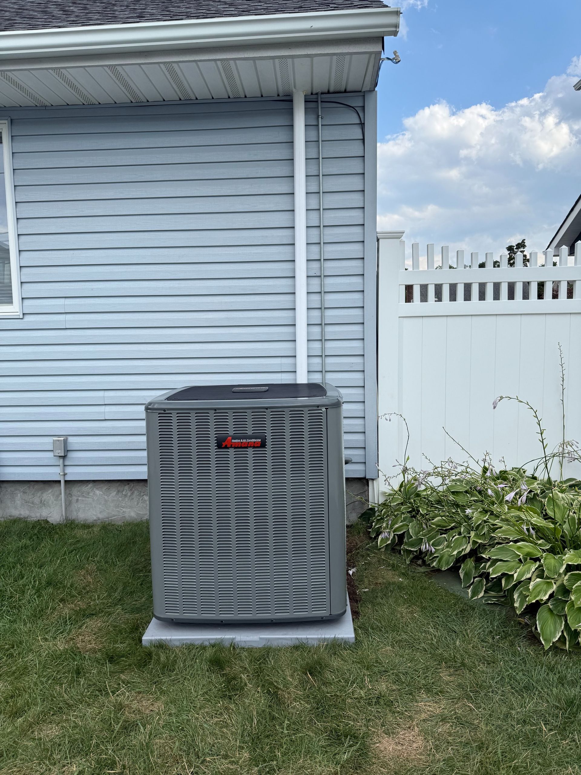 Central air conditioning unit outside a beige house with beige siding, gray unit, and conduit.