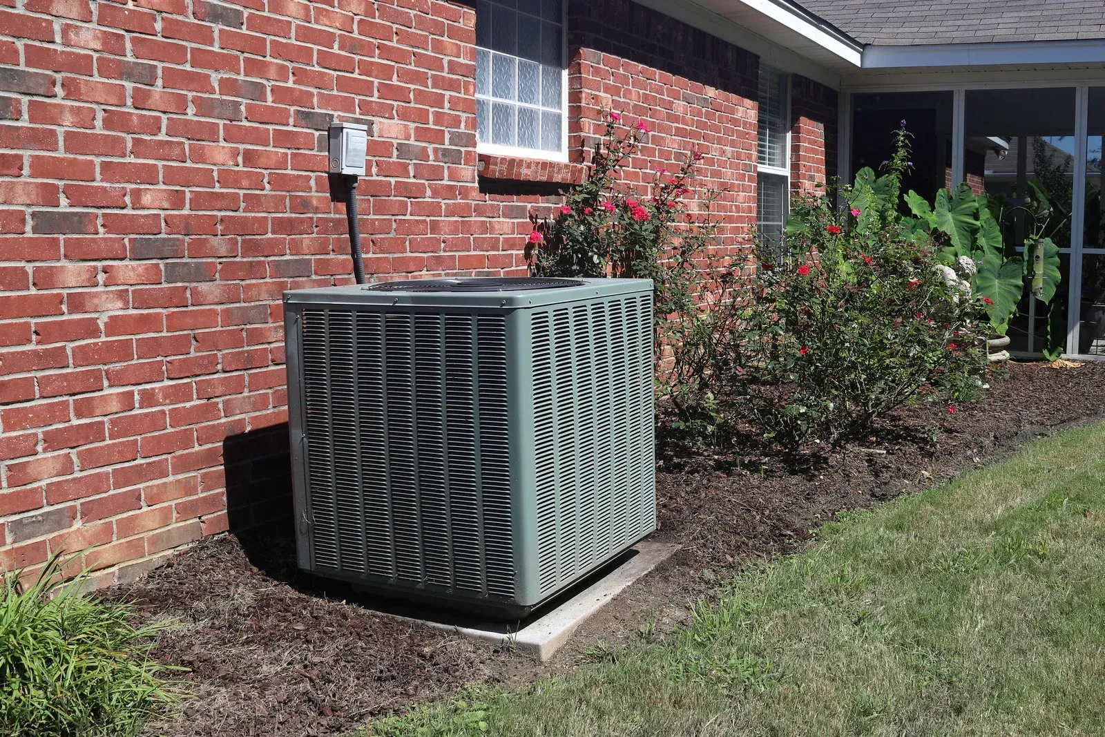 An air conditioner is sitting on the side of a brick house.