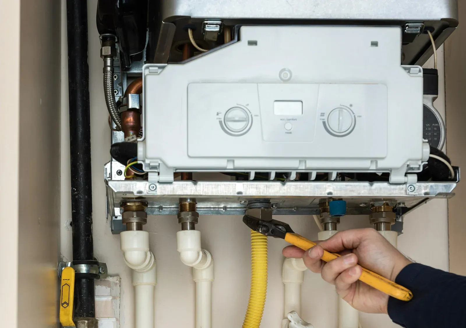 A person is fixing a boiler with a pair of pliers.