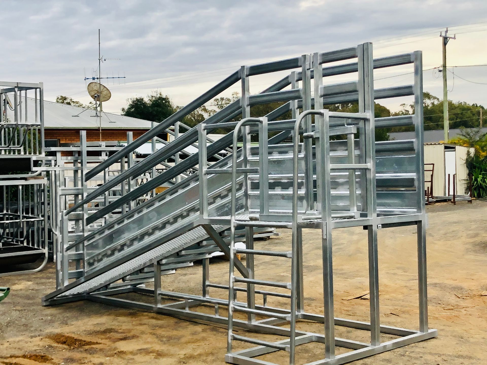 Metal cattle loading ramp on a dirt lot, featuring a sloped walkway with railings.