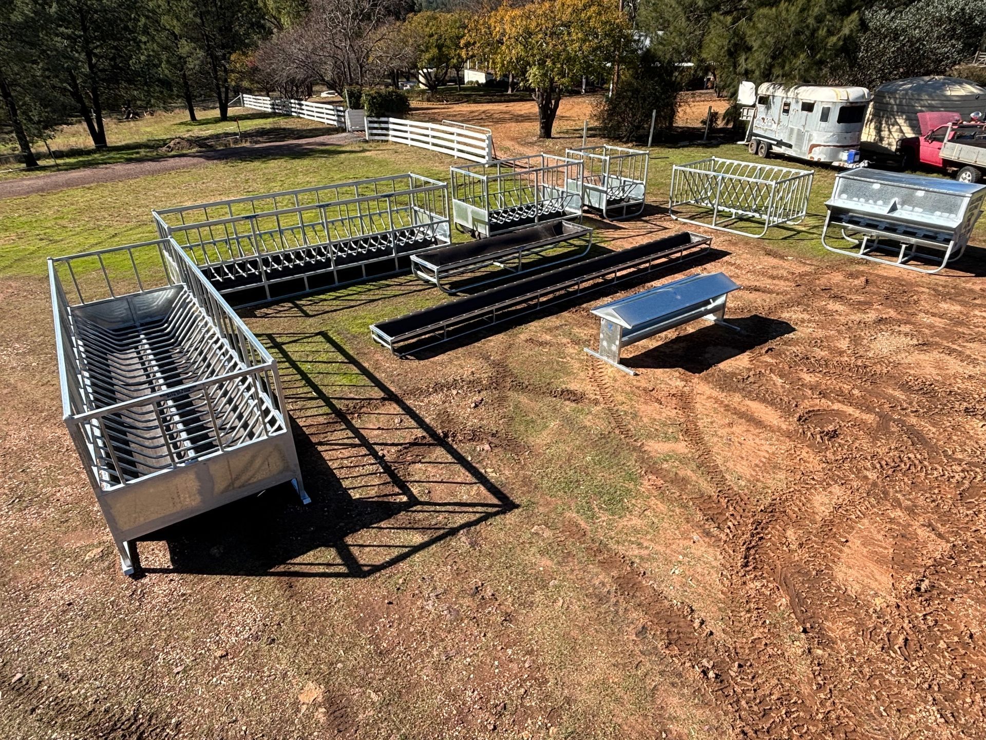Metal animal pen components sit on brown dirt, in front of a trailer and trees.