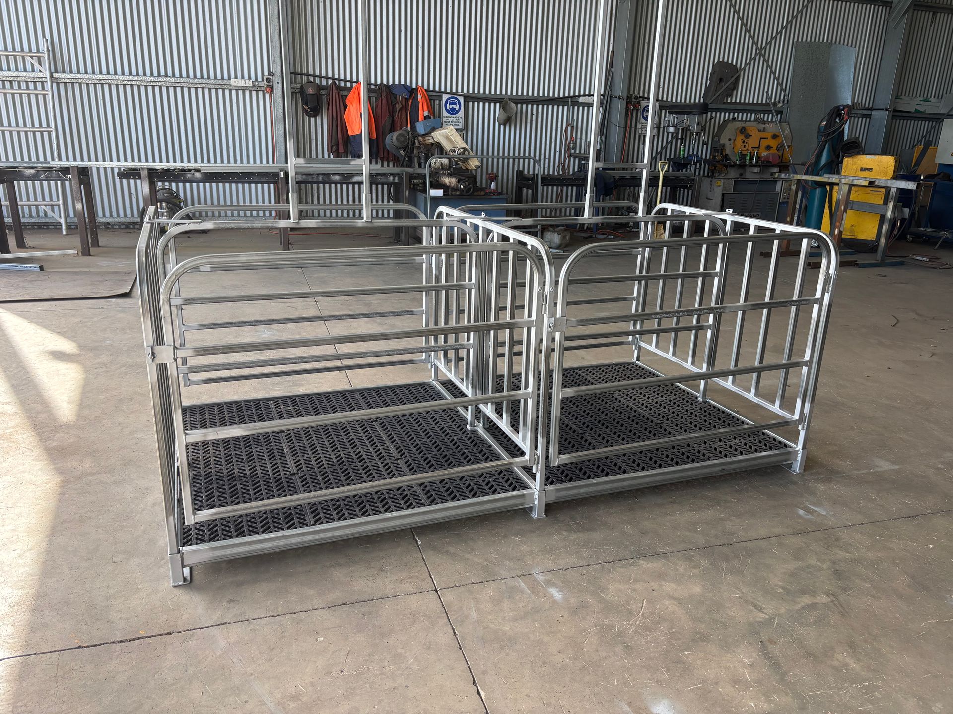 Two connected metal pens with black rubber flooring, inside a workshop.