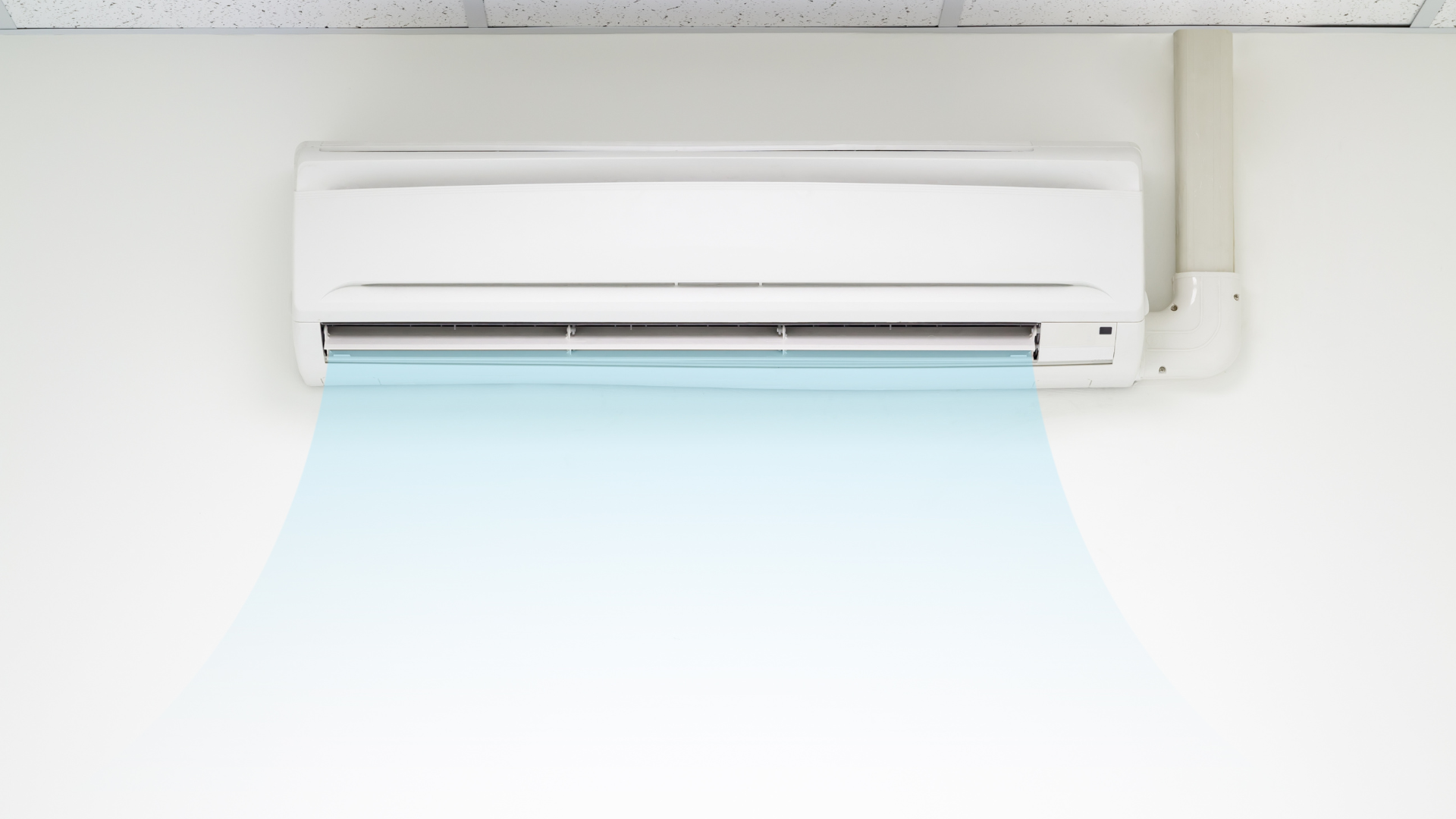 A white air conditioner is hanging on a white wall.