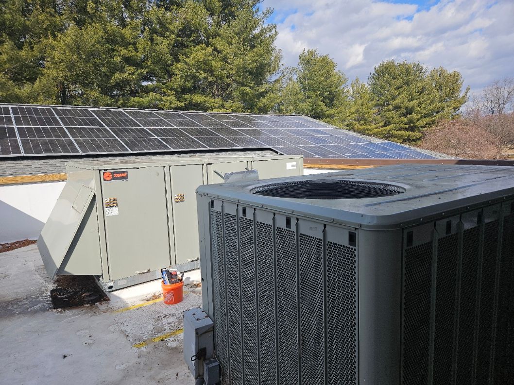 A large air conditioner is sitting on top of a snow covered roof next to a solar panel.