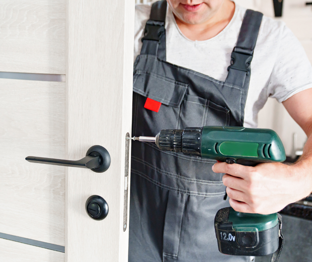 A man is using a drill to fix a door handle.