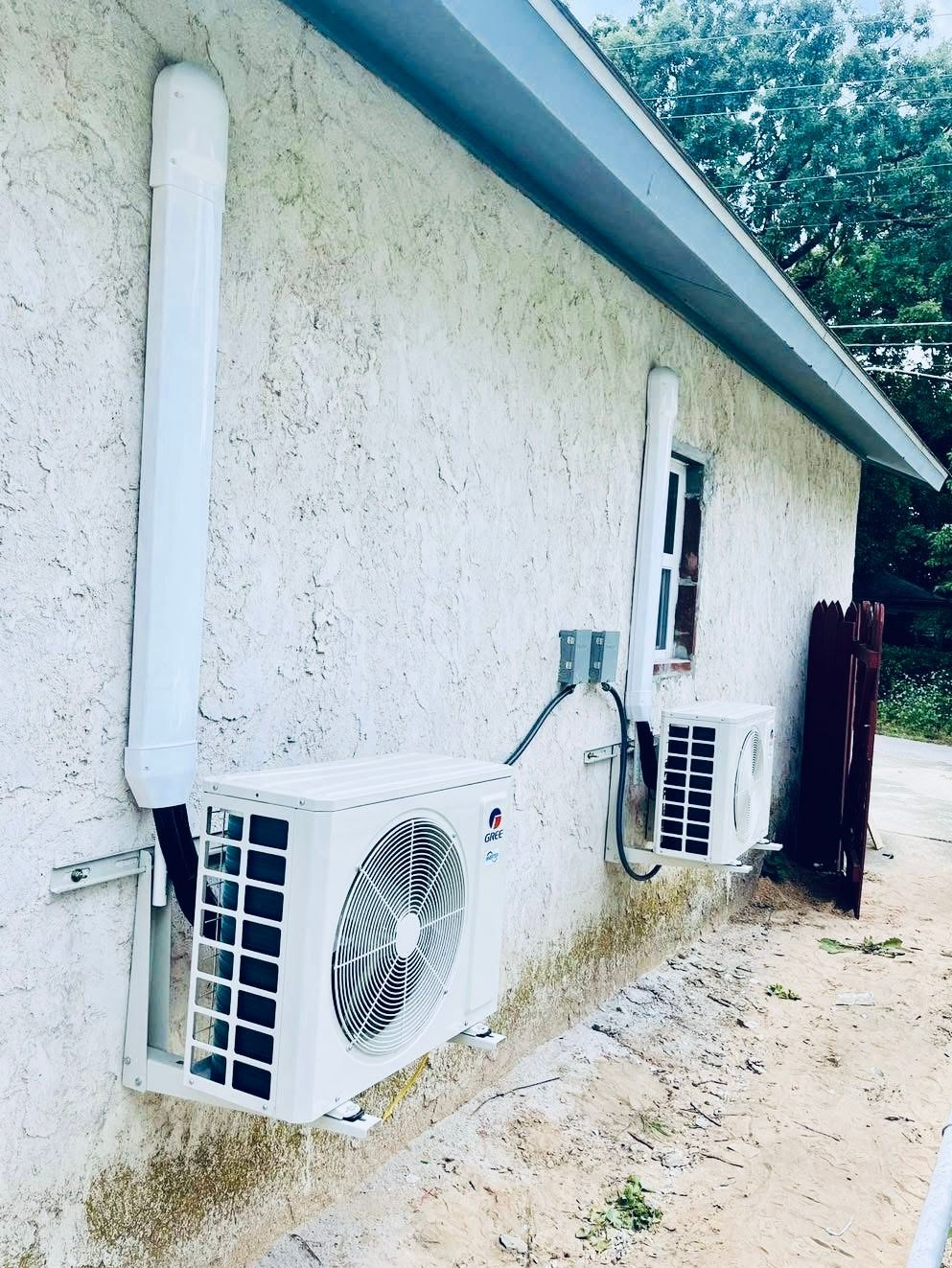 Two air conditioners are mounted on the side of a house