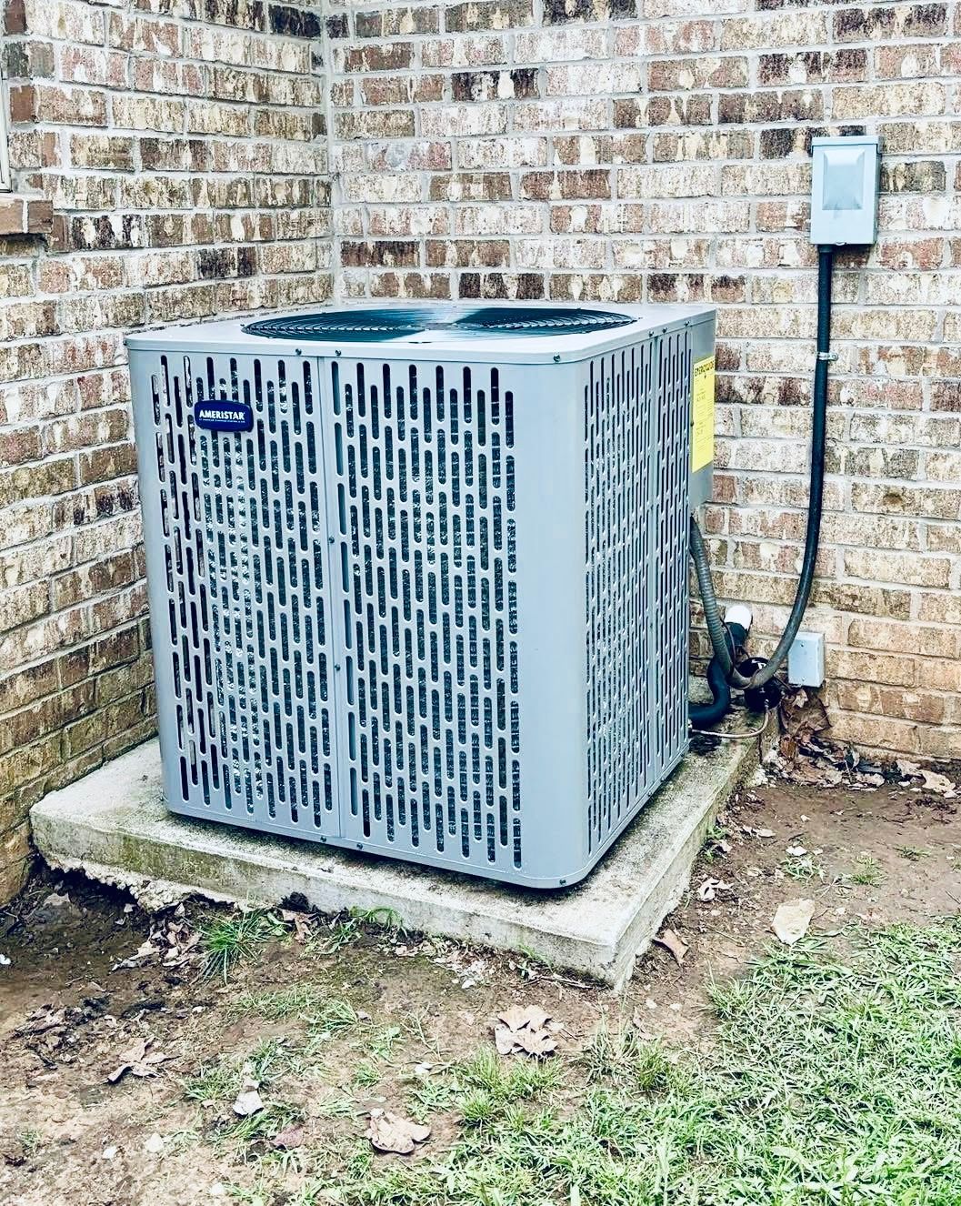 A carrier air conditioner is sitting on a concrete platform next to a brick wall.