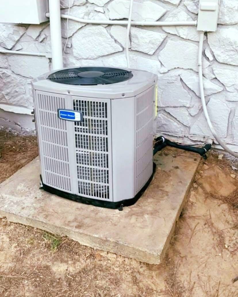 A large air conditioner is sitting on top of a concrete platform in front of a stone wall.