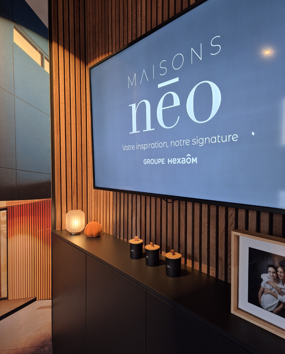 Téléviseur sur un mur en lattes de bois affichant le logo « MAISONS néo » 