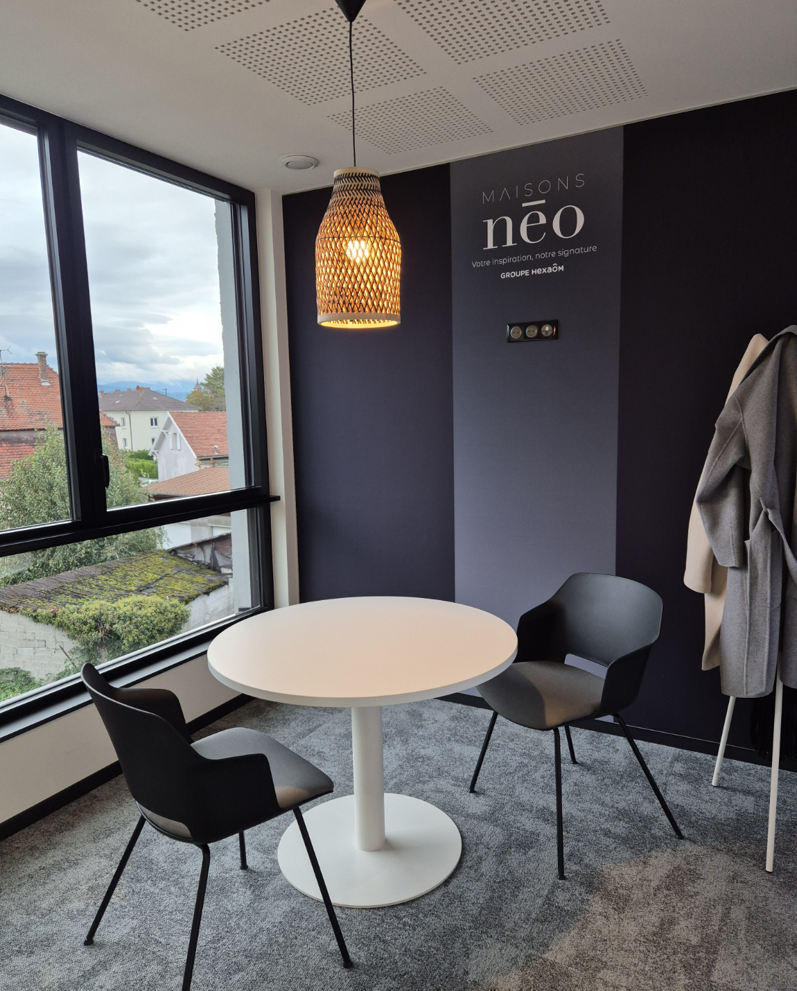 Un espace de réunion moderne avec une table ronde blanche, deux chaises, une fenêtre et une lumière suspendue.