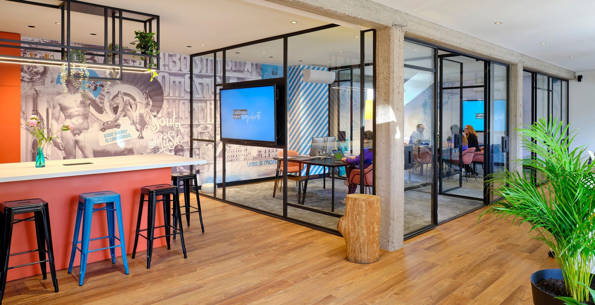 Espace de bureau lumineux avec salles de réunion vitrées, bar avec tabourets et grand écran.