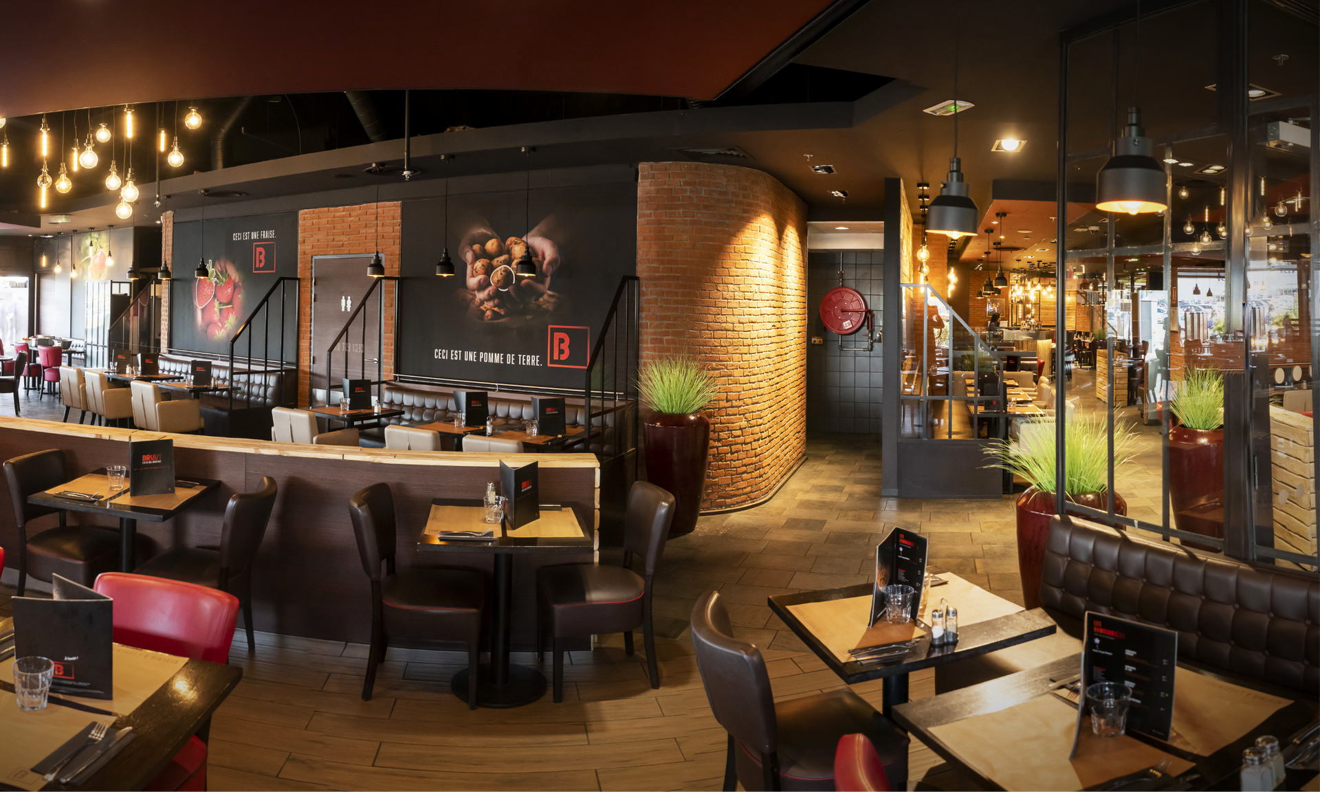 Intérieur de restaurant avec tables, chaises, briques apparentes et éclairage décoratif.