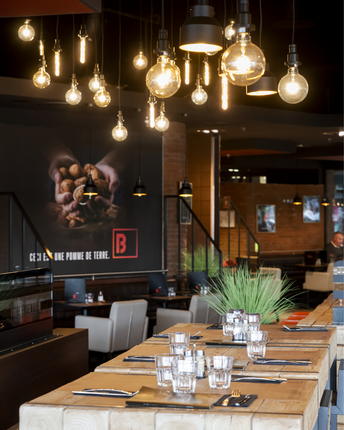 Intérieur du restaurant : table en bois , mur de briques avec une fresque sur le thème de la nourriture et coin salon.