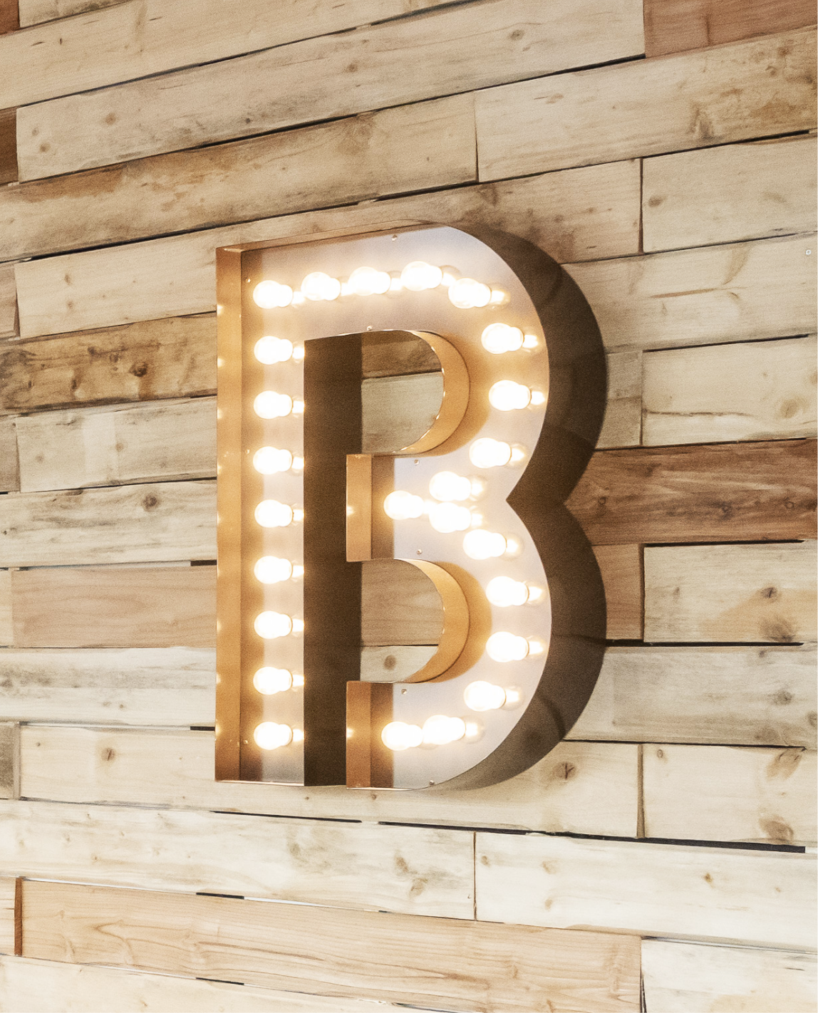 Grande lettre « B » illuminée sur un mur en planches de bois.