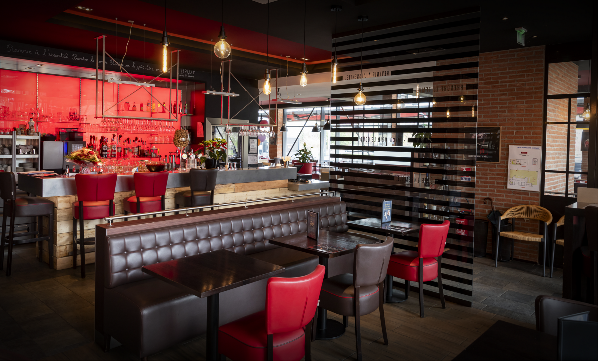 Intérieur d'un bar avec des chaises rouges, un long bar et un mur de briques.