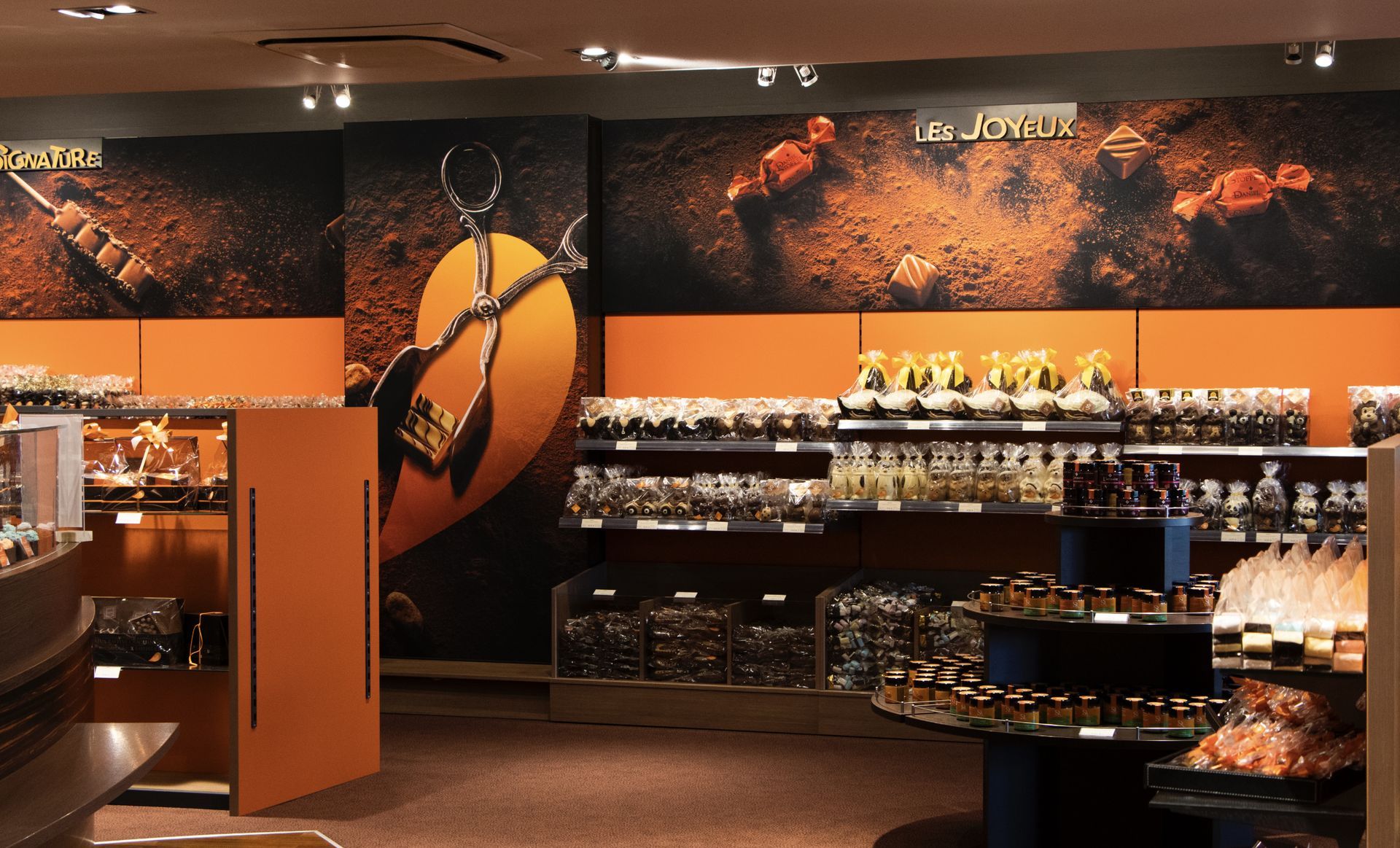 Intérieur d'un magasin. Étagères présentant les produits, murs orange et noirs et présentoir central.