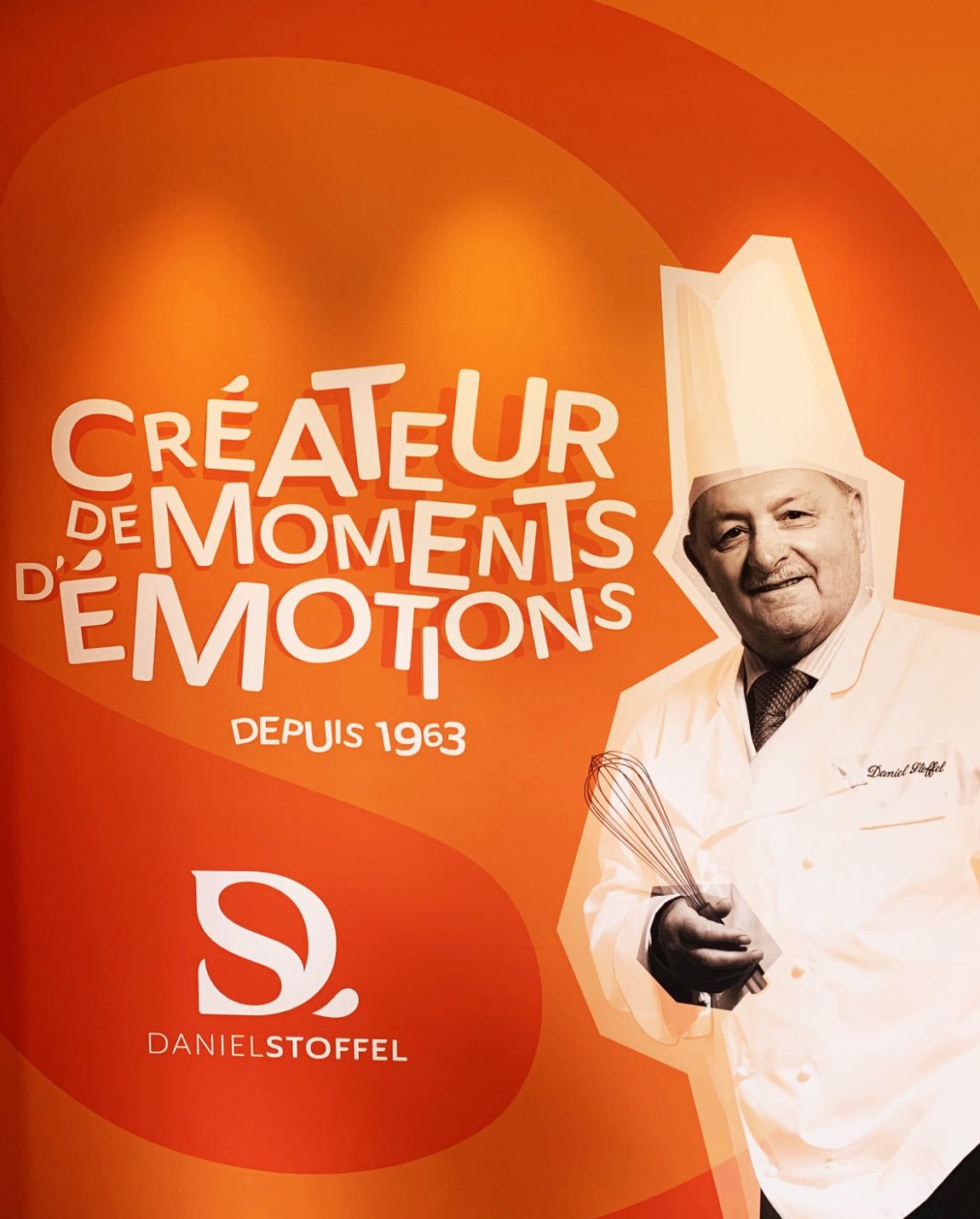 Chef en blanc, tenant un fouet, sur fond orange, texte : 