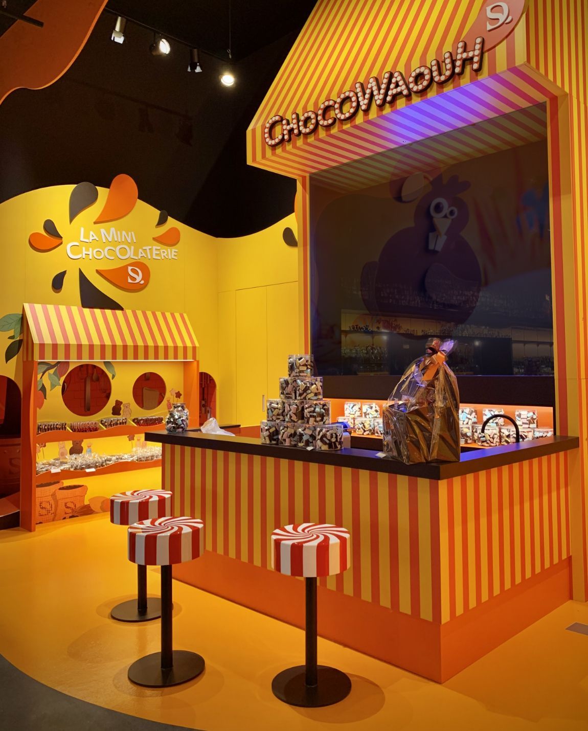 Un magasin de bonbons aux couleurs vives avec des accents rayés orange et blancs et une signalisation « ChocowDough ».