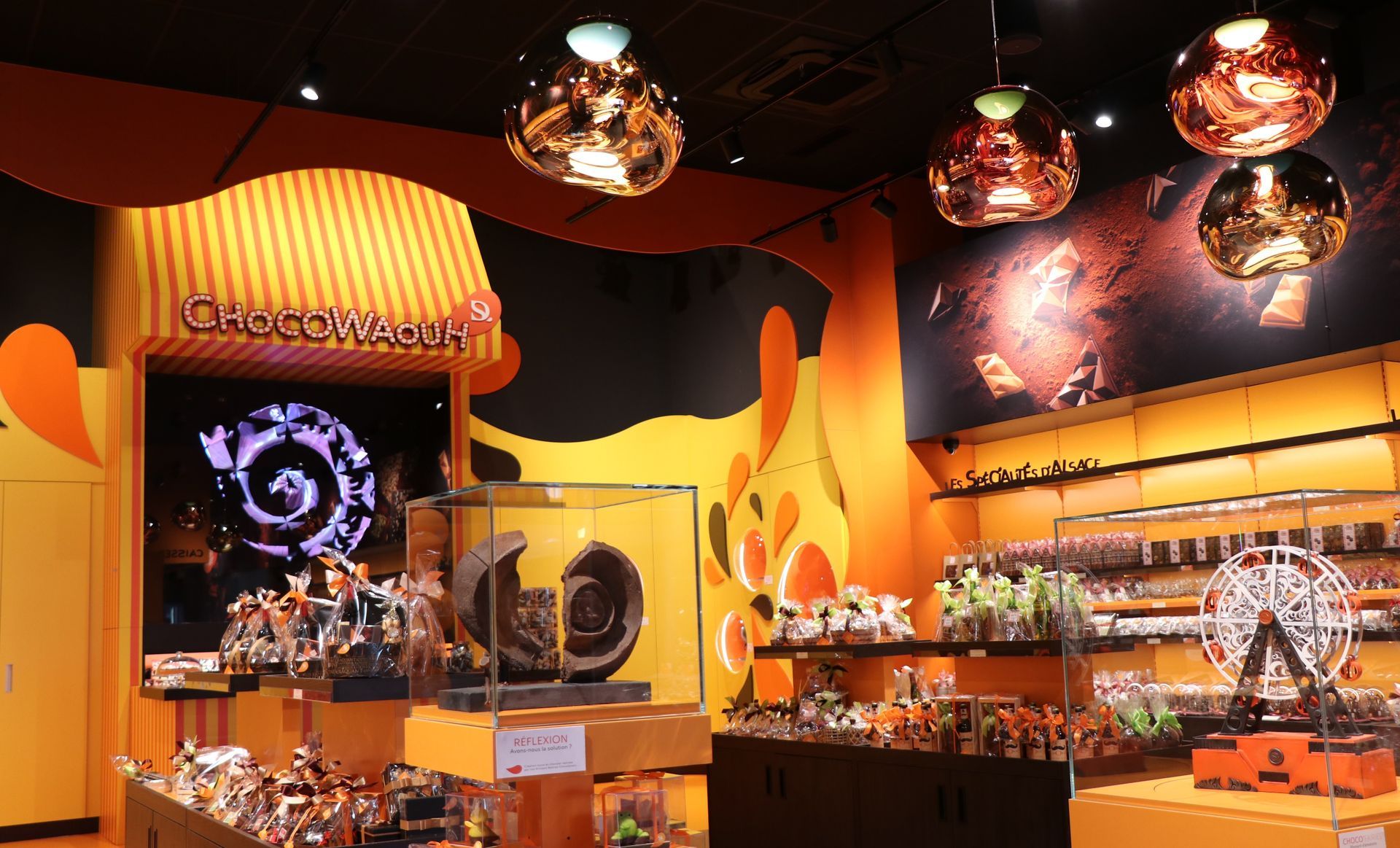 Intérieur de magasin de jouets avec décor orange et noir, étagères de présentation et lumières suspendues.