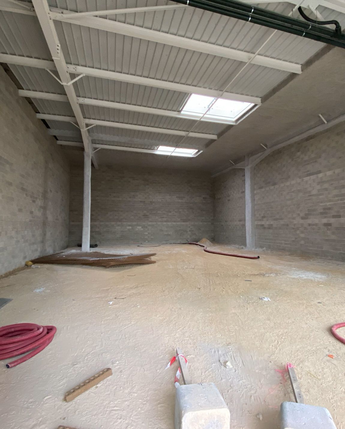 Intérieur d'entrepôt vide avec murs en béton, plafond en métal et deux puits de lumière.