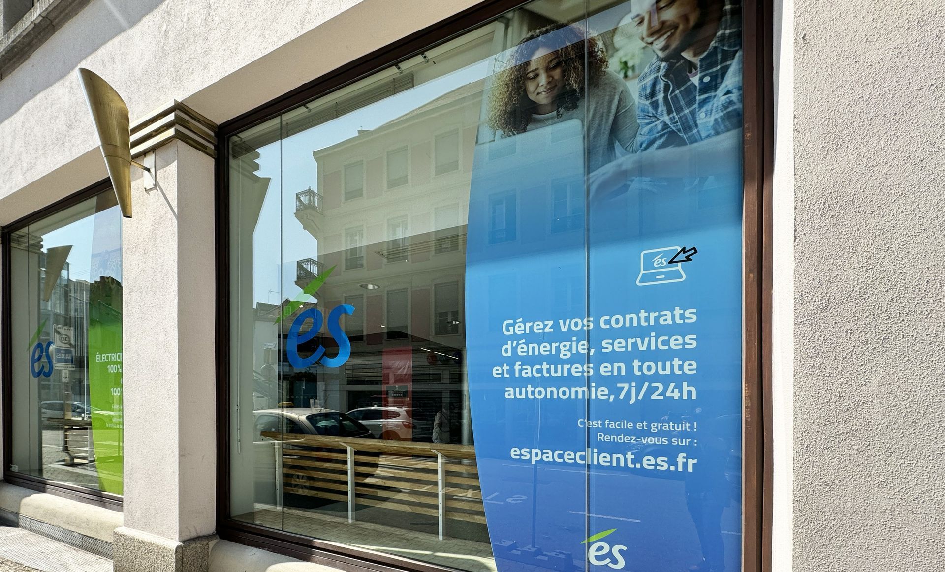 Façade de magasin avec une grande vitrine faisant la publicité de services énergétiques. Enseigne bleue et verte.