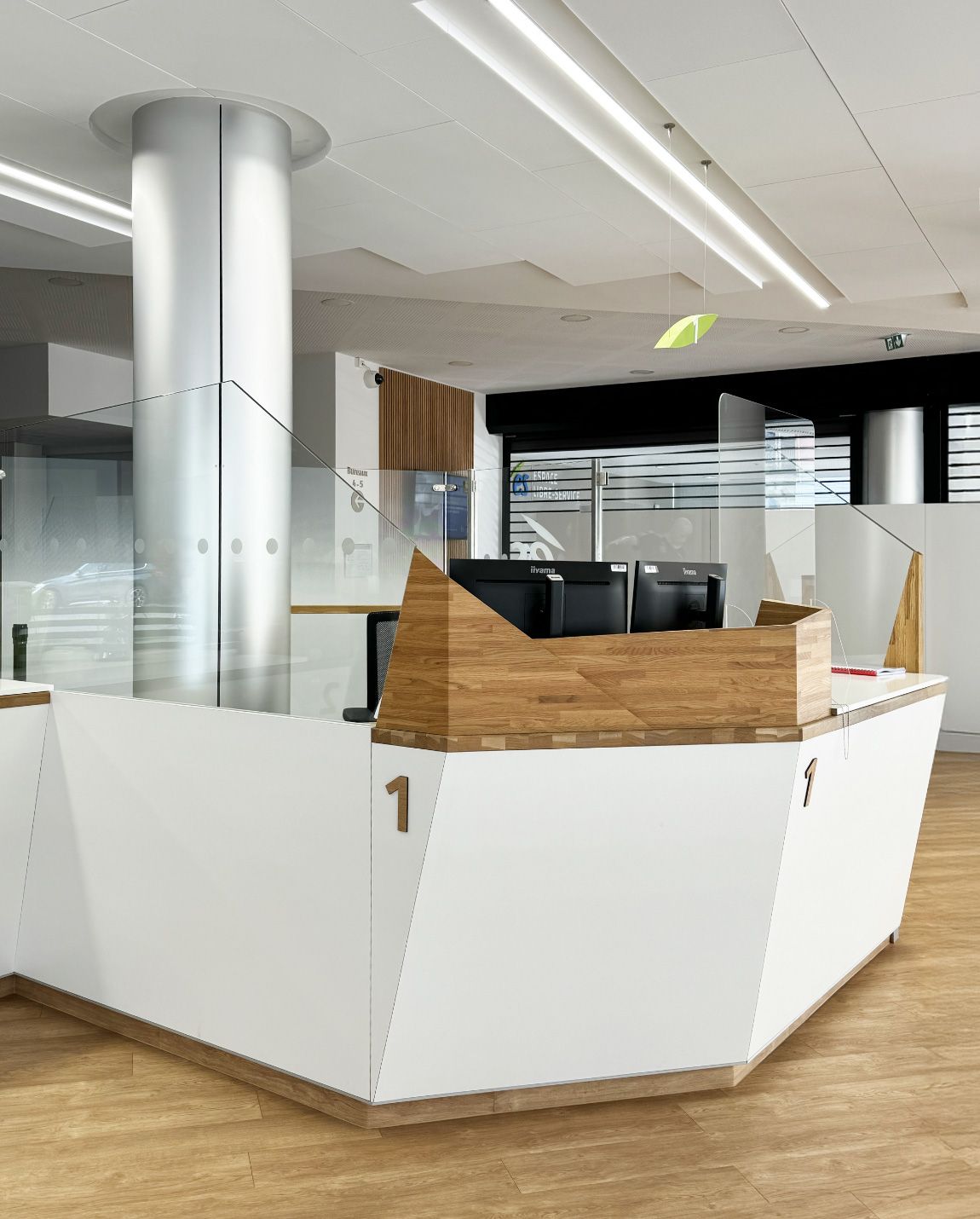 Bureau d'accueil blanc et bois au design géométrique. Des écrans sont posés dessus. Le chiffre « 1 » est visible.
