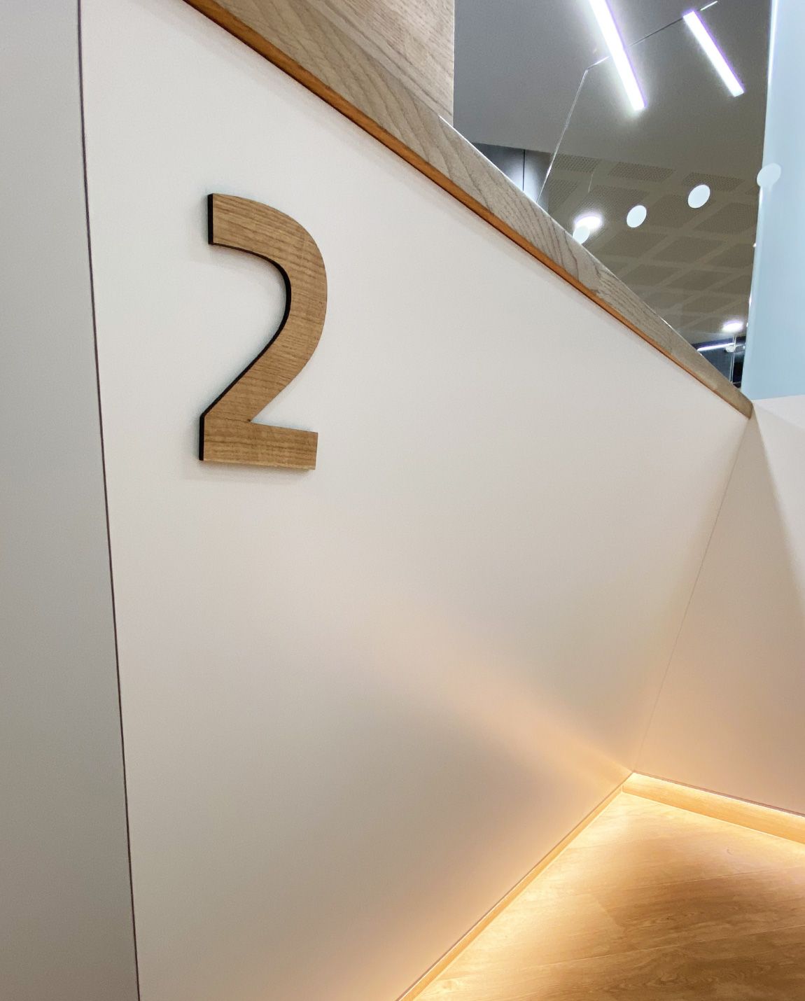 Chiffre « 2 » en bois sur un mur blanc. Le mur est orné d'une moulure en bois et d'un éclairage intégré en dessous.