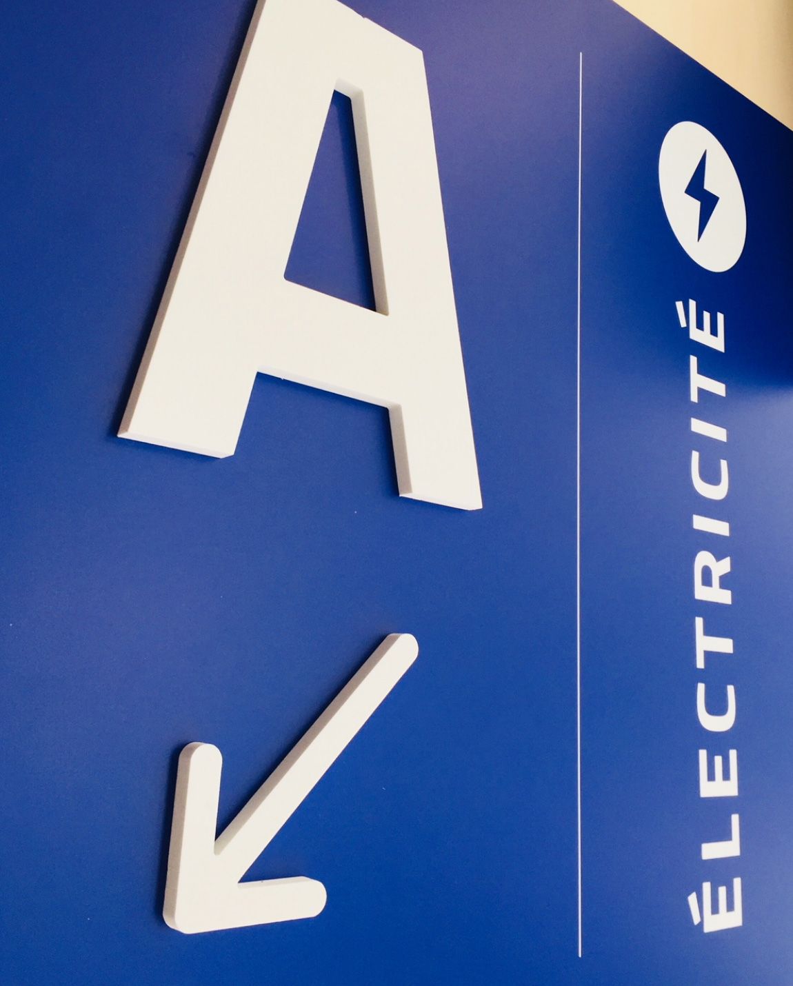 Un « A » blanc et une flèche pointent vers le panneau « Électricité » orné d'un éclair sur un mur bleu.