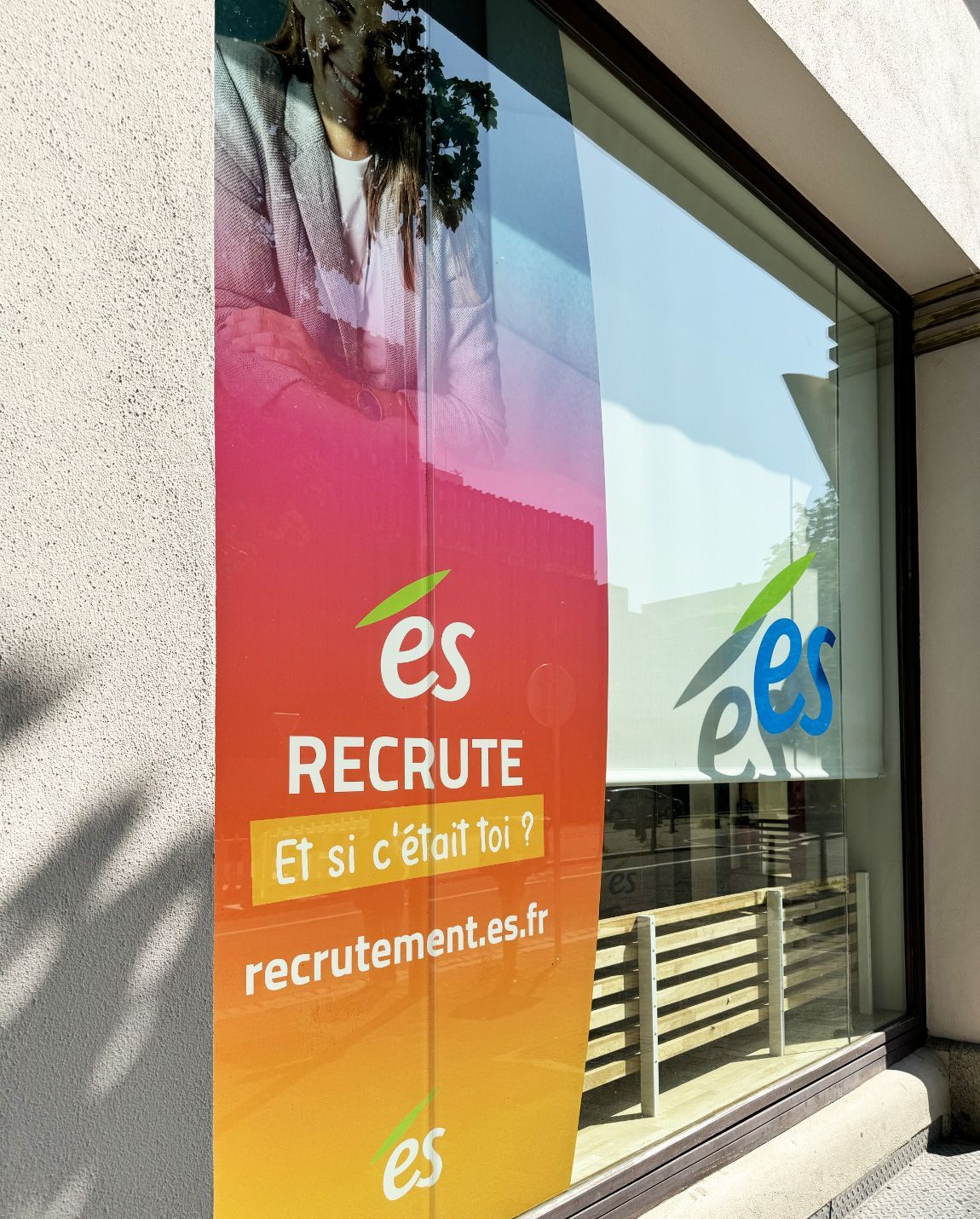 Vitrine avec annonce de recrutement ; bannière colorée, « ES RECRUTE ».