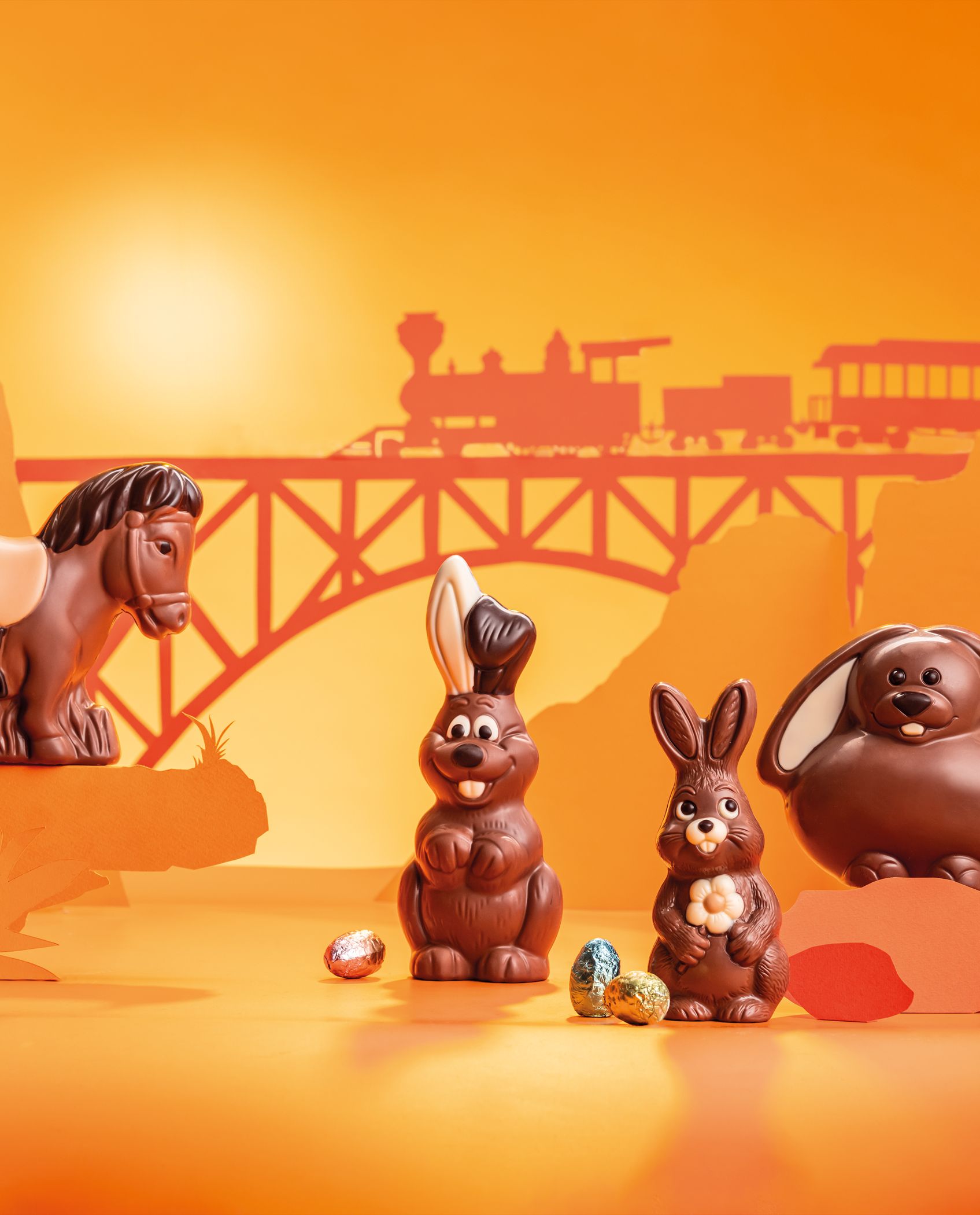Lapins de Pâques en chocolat et figurines de chevaux dans un décor de désert orange, avec un train sur un pont.