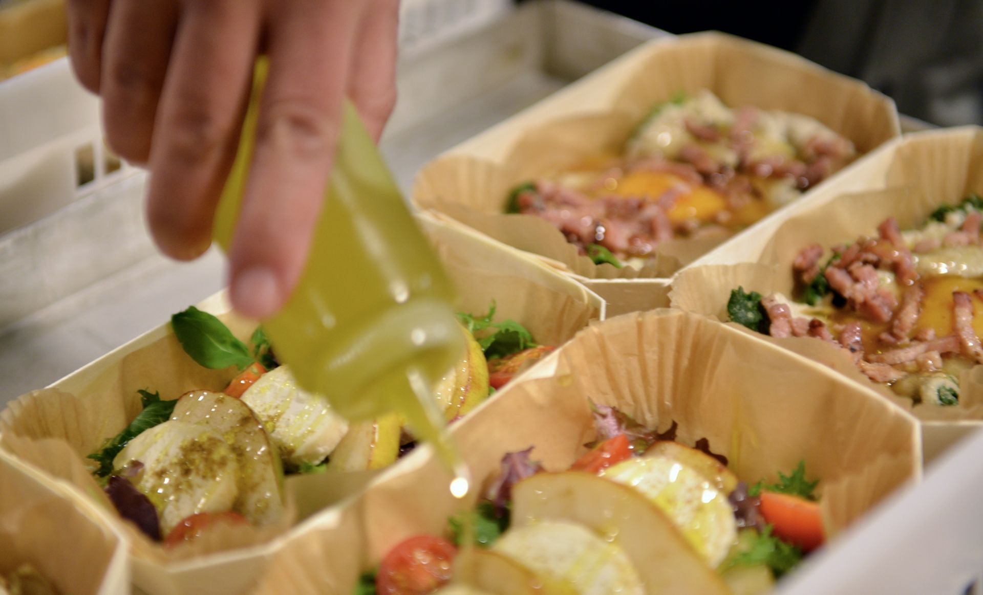 Une personne versant de la vinaigrette sur des salades et des plats à base d'œufs dans des récipients en bois.