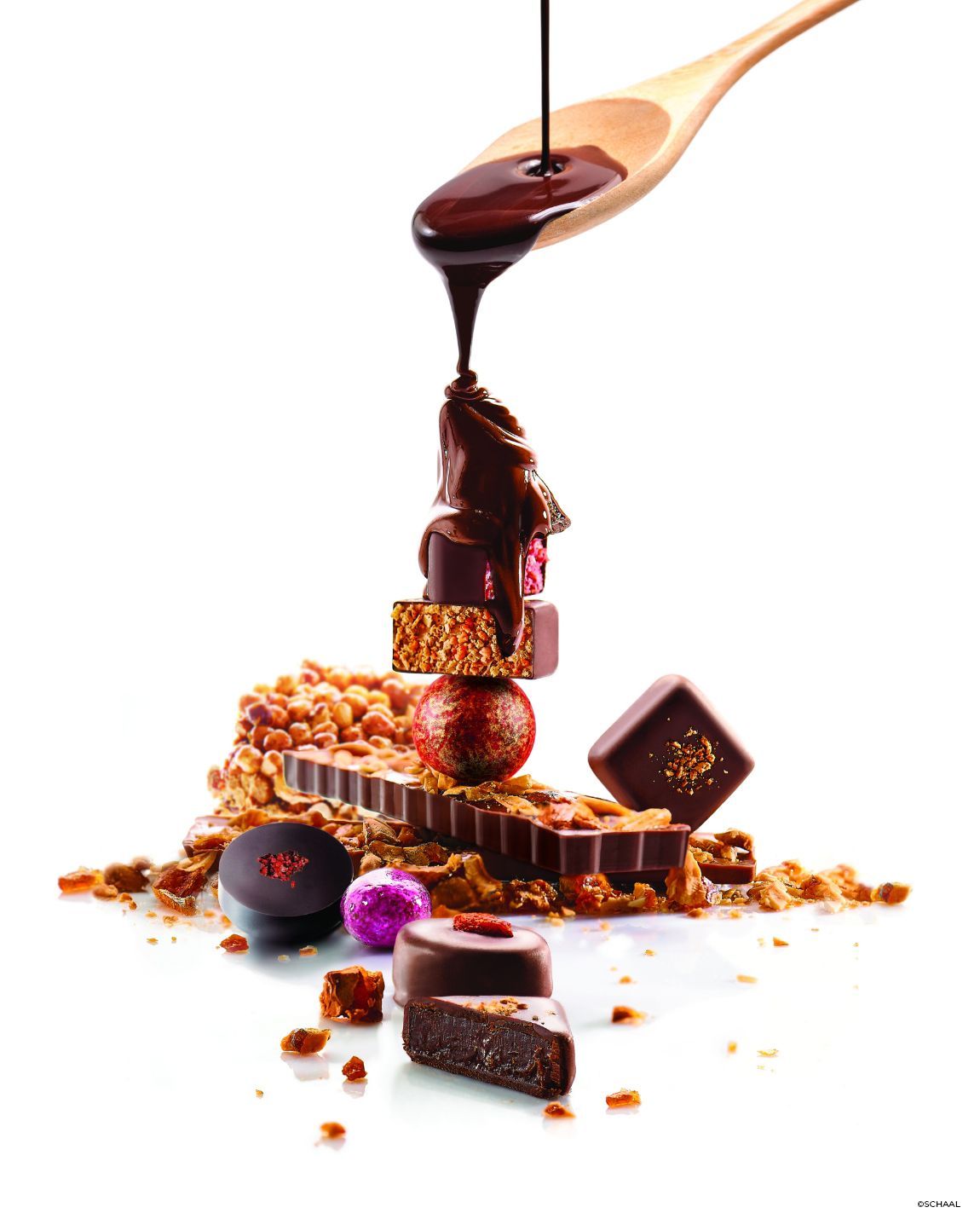 Du chocolat versé à l'aide d'une cuillère en bois sur une tour de chocolats et de friandises.