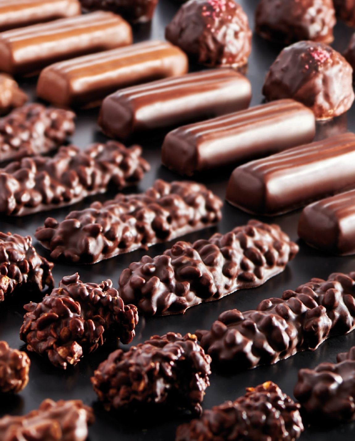 Assortiment de bonbons au chocolat sur une surface sombre, présentant des formes et des textures variées, dans des tons de brun.