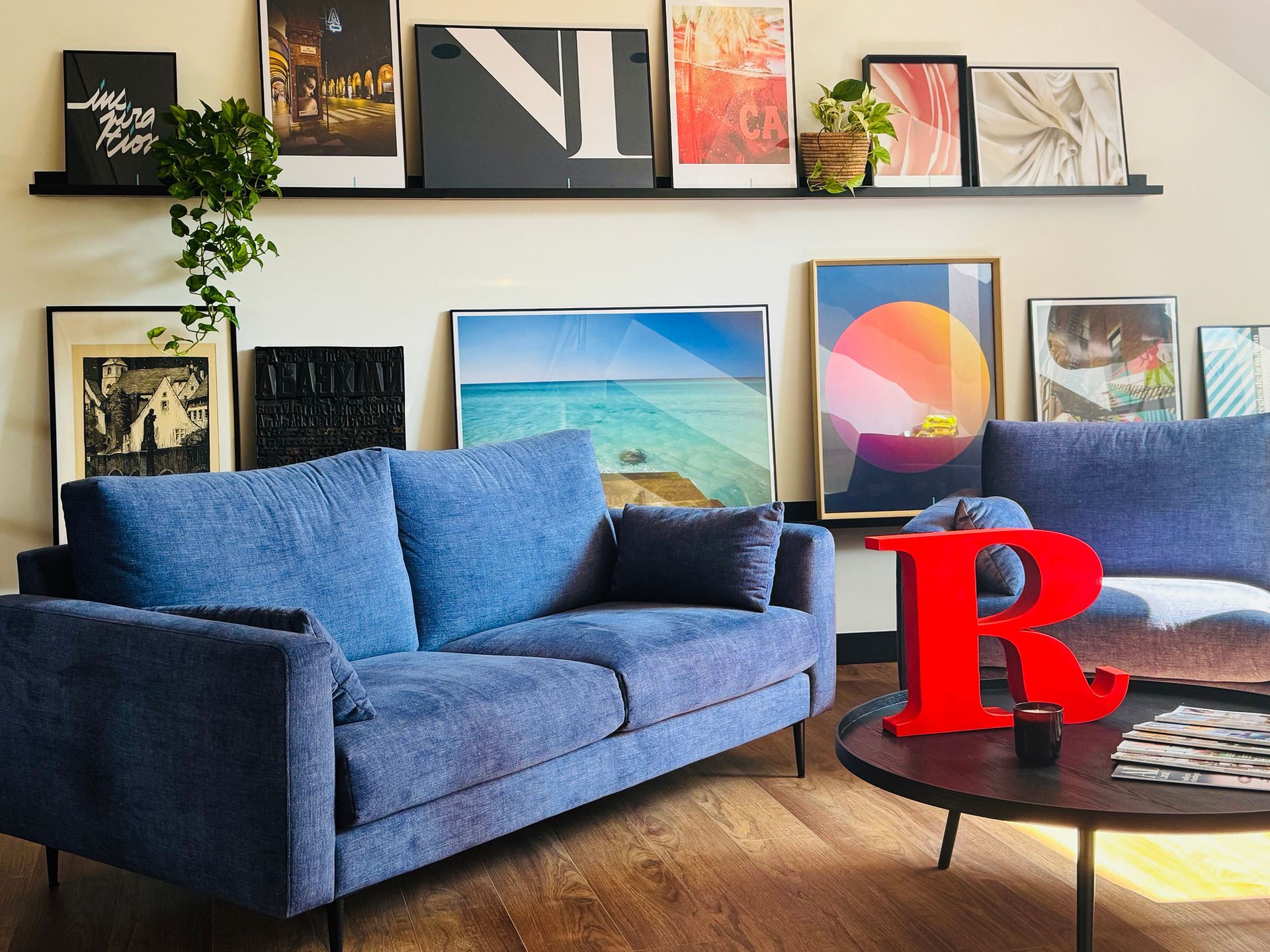 Un canapé bleu dans une pièce avec de l'art, une table ronde et une grande lettre rouge « R ».