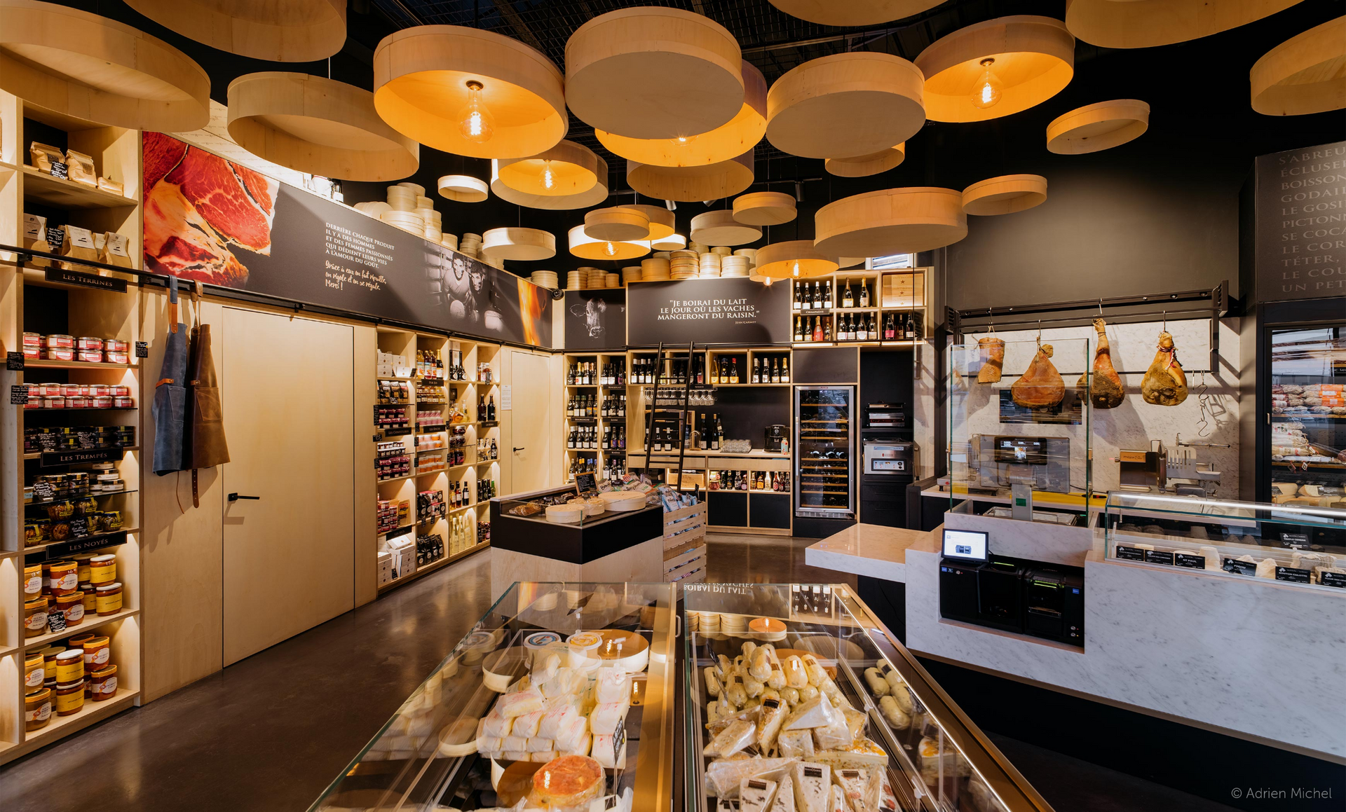Intérieur d'une épicerie fine avec des présentoirs de nourriture, de vin et des luminaires uniques.