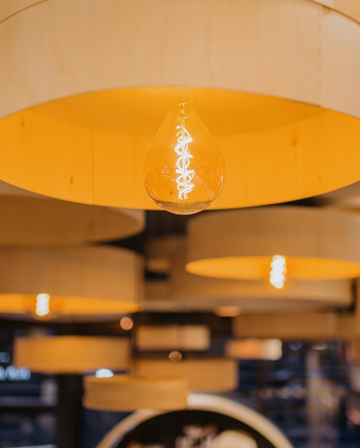 Des ampoules aux tons chauds sont suspendues à des abat-jour en bois dans un décor de restaurant.