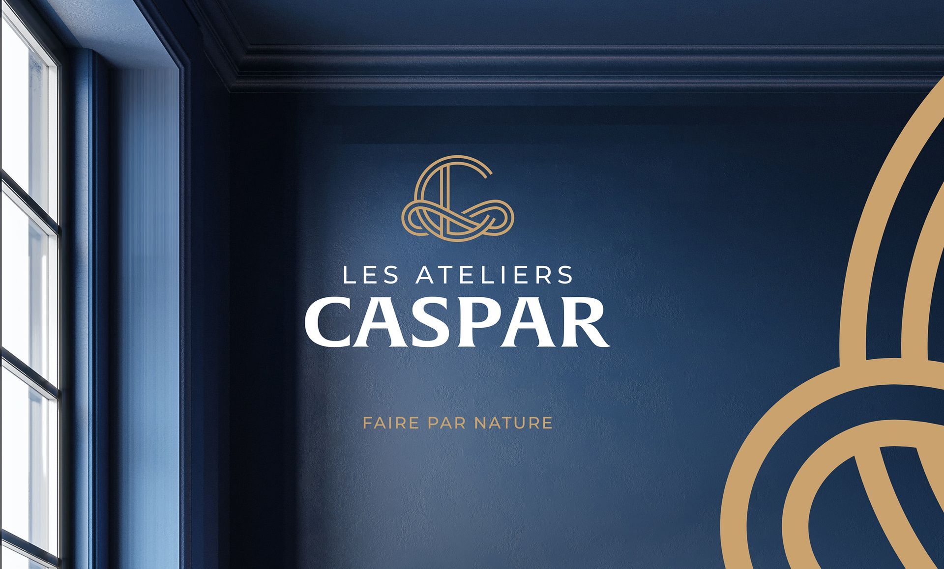 Logo des Ateliers Caspar en or et blanc sur un mur bleu marine ; une fenêtre se trouve à gauche.