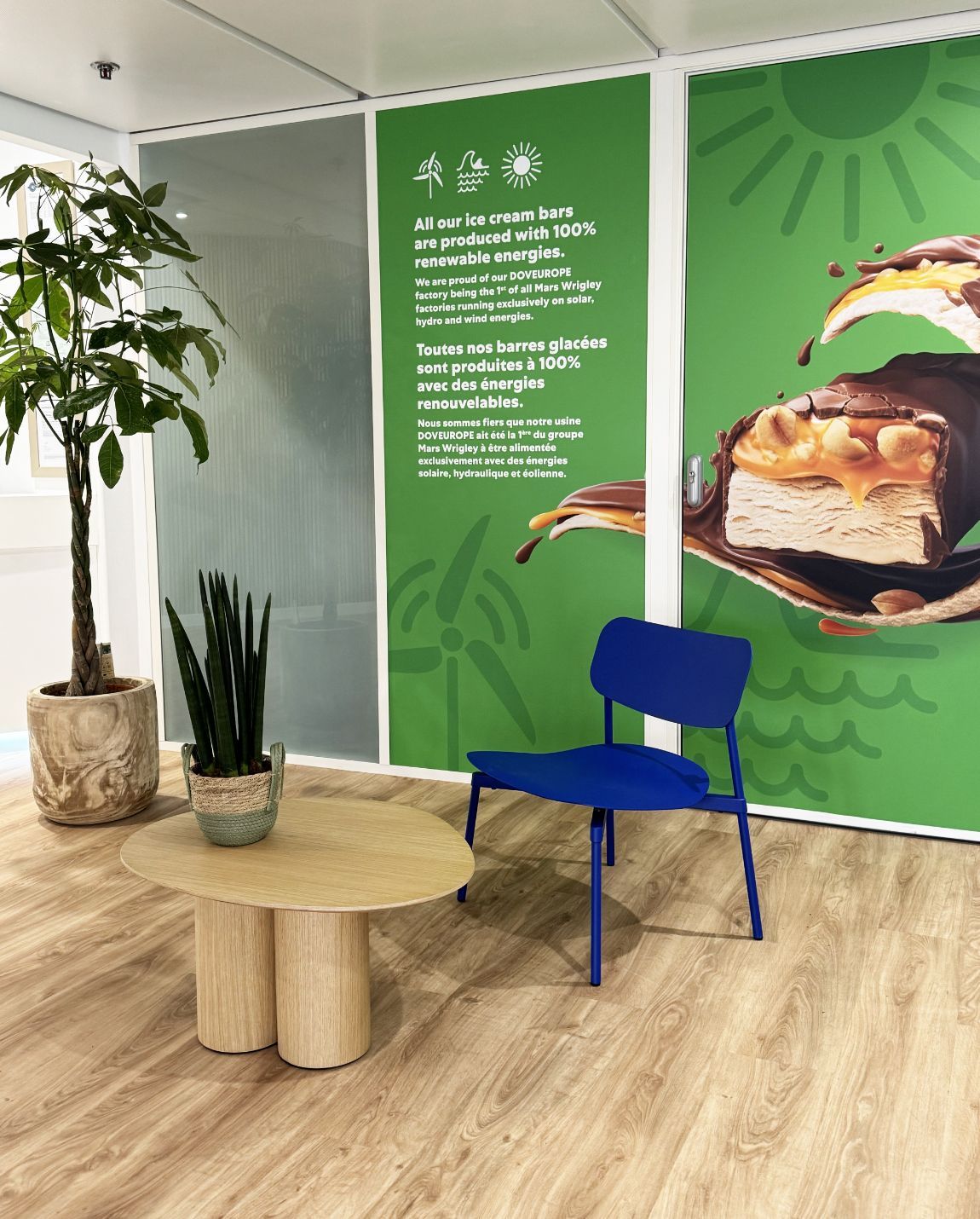Une pièce avec une chaise bleue, une petite table et une plante contre un mur vert avec une image de produit.